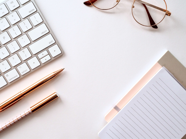 Workspace with glasses, pens, keyboard, and notepad